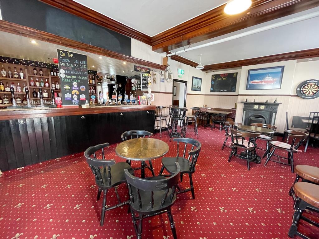 Lot: 109 - PUB WITH COURTYARD GARDEN AND FLAT ABOVE IN COASTAL TOWN - Main bar area with tables chairs fireplace and dart board